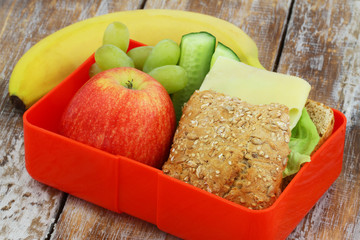 Healthy lunch box consisting mixed grain cheese roll, apple, grapes and banana
