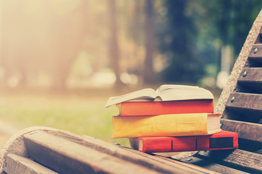 Stack of hardback books and Open book lying on bench at sunset park against blurred nature backdrop. Copy space, back to school. Education background. Toned image
