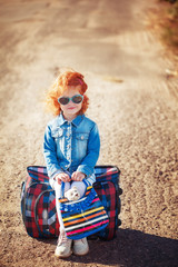 Cute little girl is having fun on suitcase in sunny day. Travel