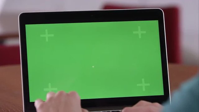 Panning shot of woman using computer with green screen.