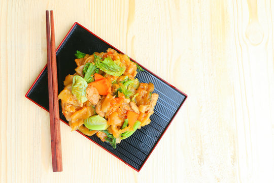 Noodle in black plate with chopsticks on wooden background
