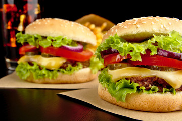 Cheeseburgers,french fries and cola on wooden desk on black