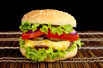 Big cheeseburger on wooden mat on black background
