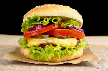 Big cheeseburger on wooden board on black background
