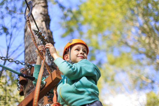 cheerful and brave boy at a height. child enjoys the view from the top in the ropes course and prepare for extreme downhill