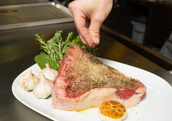 Uncooked T Bone being seasoned with olive oil, black pepper, rosemary and garlic.
