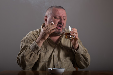 Alcoholism: portrait of a lonely, desperate man drinking alcohol and smoking cigarette