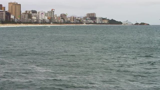 Wide shot of open ocean and surfers with City.