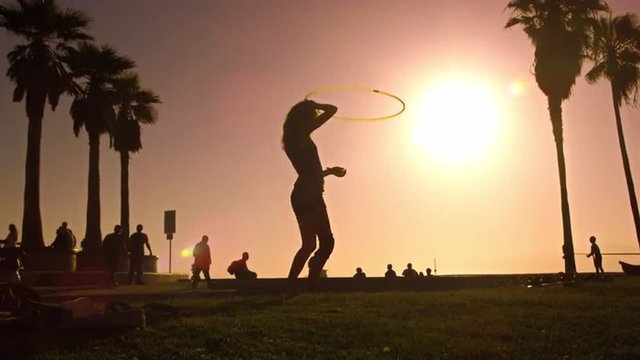Slow motion shot with lens flare of a woman playing with a hula hoop near Venice Beach, California