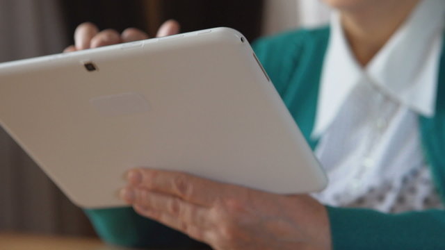 Close up of a white tablet PC in a mature woman hands - Side view
