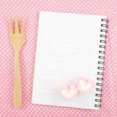 The lovely pink heart marshmallows and small white note book and wooden fork on pink cotton fabric for Valentine's day.