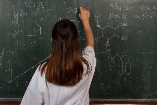 Young Female Scientist Writing Molecular Structure On Green Board