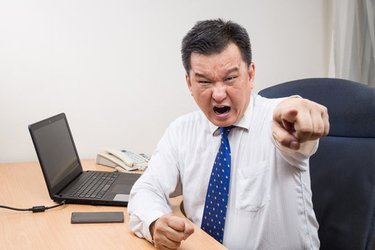 Angry and stressful Asian manager shouting and pointing in office