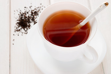 tea in a white mug with a spoon and tea leaves on a white background