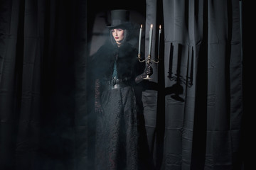 Witch gothic fashion woman wearing black cape and hat. Holding c