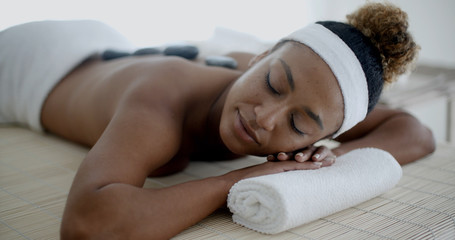 African american woman relaxing at a health spa while having a hot stone treatment