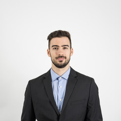 Head and shoulder front portrait of young man in suit and blue shirt looking at camera. Portrait over gray studio background