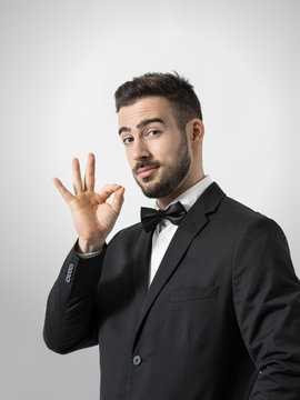 Young bearded restaurant waiter showing delicious hand gesture looking at camera. Desaturated portrait over gray studio background with retro vignette. 
