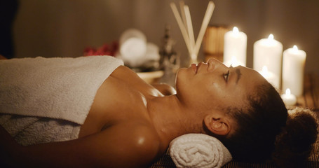 Young woman getting relaxing in the spa salon with candles on the background