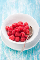Fresh raspberries in a white ceramic bowl with metal spoon. closeup, selective focus..