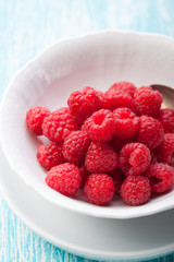 .Fresh raspberries in a white ceramic bowl with metal spoon. closeup, selective focus.
