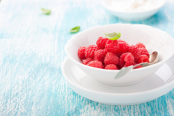 Fresh raspberries in a white ceramic bowl with metal spoon. closeup, selective focus.