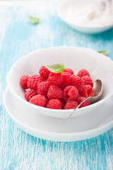 Fresh raspberries in a white ceramic bowl with metal spoon. closeup, selective focus.