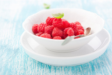Fresh raspberries in a white ceramic bowl with metal spoon. closeup, selective focus