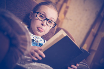 Girl reading a book at home sitting in an armchair.