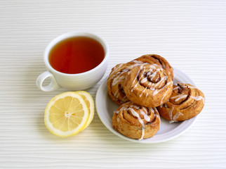 sweet buns with cinnamon on a plate witn cup of tea and lemon