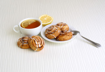sweet buns with cinnamon on a plate witn cup of tea and lemon