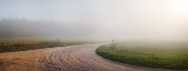 Landscape with an old gravel road in the fog. Turn of gravel road. Panoramic shot. Toned image.