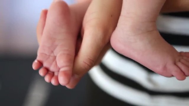 A close up shot of an young adult's hand holding two of a baby's feet.