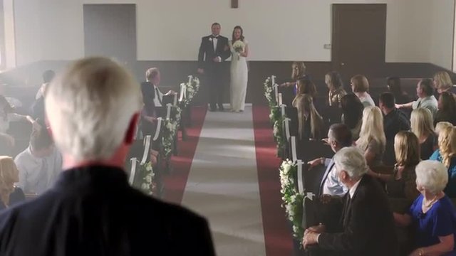 Father walking bride to the preacher at the front of a chapel.