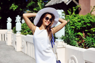 Beautiful young woman in elegant hat and sunglasses posing outdo