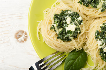 Italian pasta with spinach and feta on green plate on the wooden background.