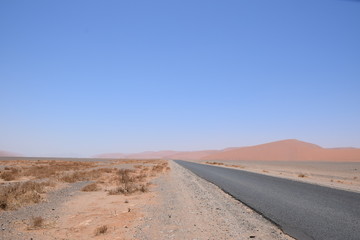 Straße in der Wüste mit Dünen im Hintergrund