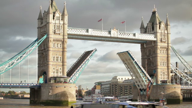Boat passes through Tower Bridge with bascules raised, other boat in foreground, located in London, England.