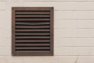 Ein altes Lüftungsgitter in einer hell angestrichenen Ziegelwand