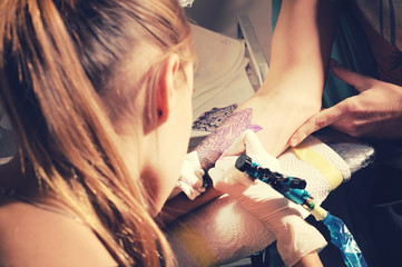 Woman tattoo master make tattoo on a hand against purplish blue likeness of a future tattoo.