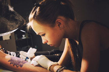 Portrait of a young cute woman master tattooist makes the tattoo on hand on a purplish blue...