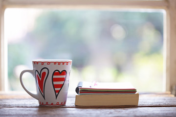 Heart pattern white cup  and notebooks at windows