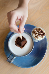 Hot cocoa served with hot milk , cocoa stick and a glass of whipped cream on a blue plate.