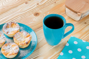 ruddy cheesecakes on blue plate, black tea in blue cup, blue napkin at white polka dots on wooden table