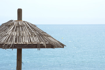 summer postcard. Straw umbrella in the sand, blue sea and summer day. copyspace on the right side.