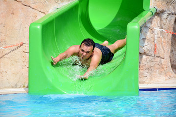Young man riding down a yellow water slide .Man enjoying a water tube ride