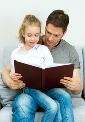 Father reading book with daughter at home.