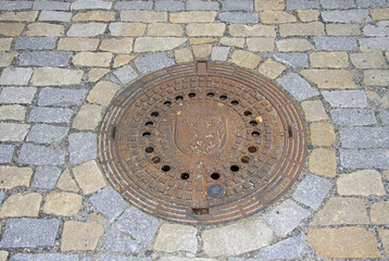 KUTNA HORA, CZECH REPUBLIC - APRIL 29, 2013: Round steel sewer manhole on old cobblestone road in Kutna Hora, Czech Republic