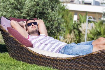 handsome young man enjoying the summer holiday relaxing on a sunbed in a green garden - obrazy, fototapety, plakaty