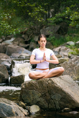 Beautiful young woman meditating in yoga pose at a mountain stream.